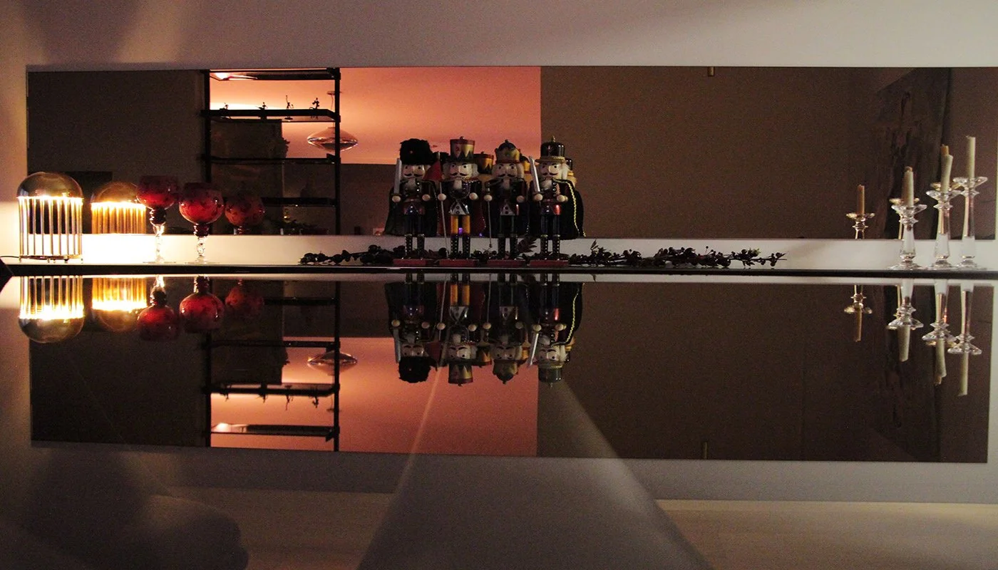 Decorative items on a reflective surface including candle holders, nutcracker figurines, and red glassware, with a mirror reflecting the objects and ambient lighting.