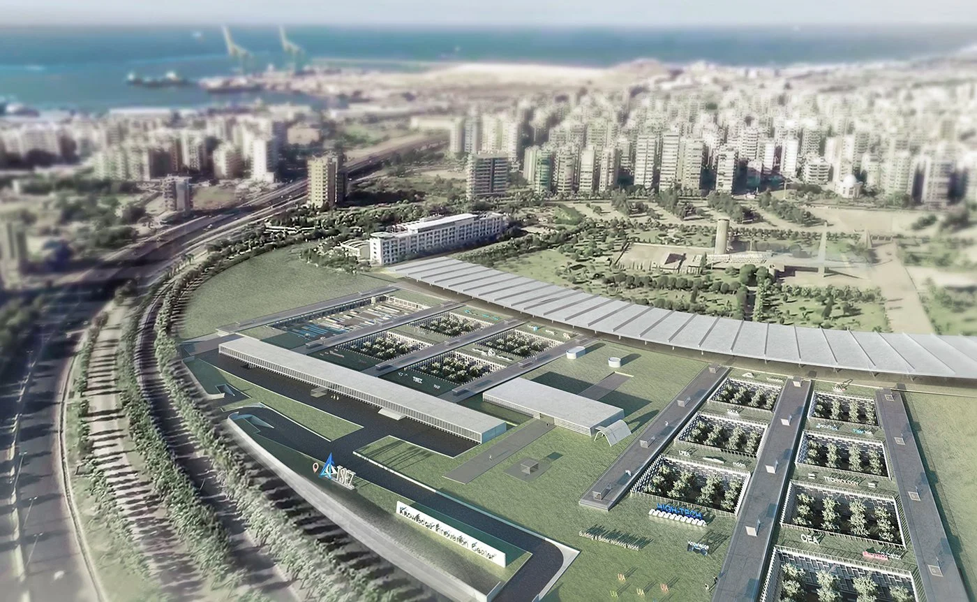 Aerial view of a modern urban development with green spaces, buildings, and water features near a coastline with sailboats.