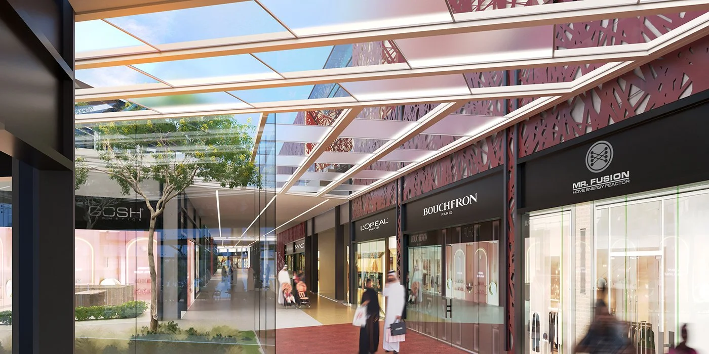 Interior view of a modern shopping mall corridor with storefronts for brands like L'Oreal, Bouchon Paris, Mr. Fusion, and Hush Cosmetics, featuring a glass ceiling and ongoing foot traffic.