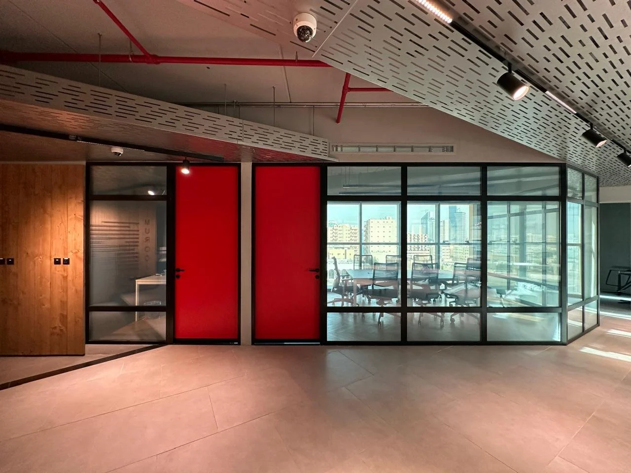 Modern office conference room with glass walls, chairs around a table, and city skyline view through large windows.