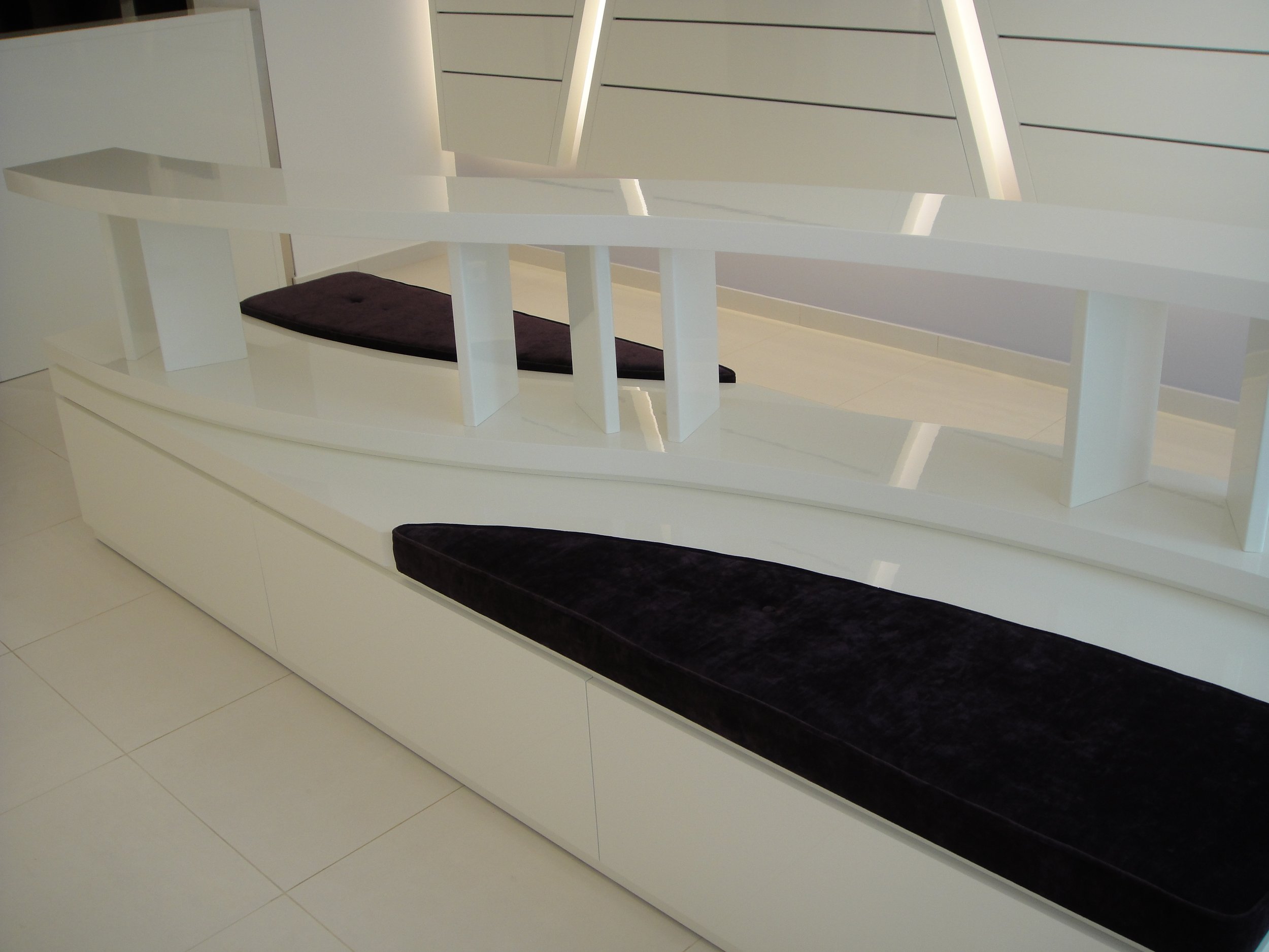 A modern white bench with a black cushion in a room with white walls and light-colored tiled floor.