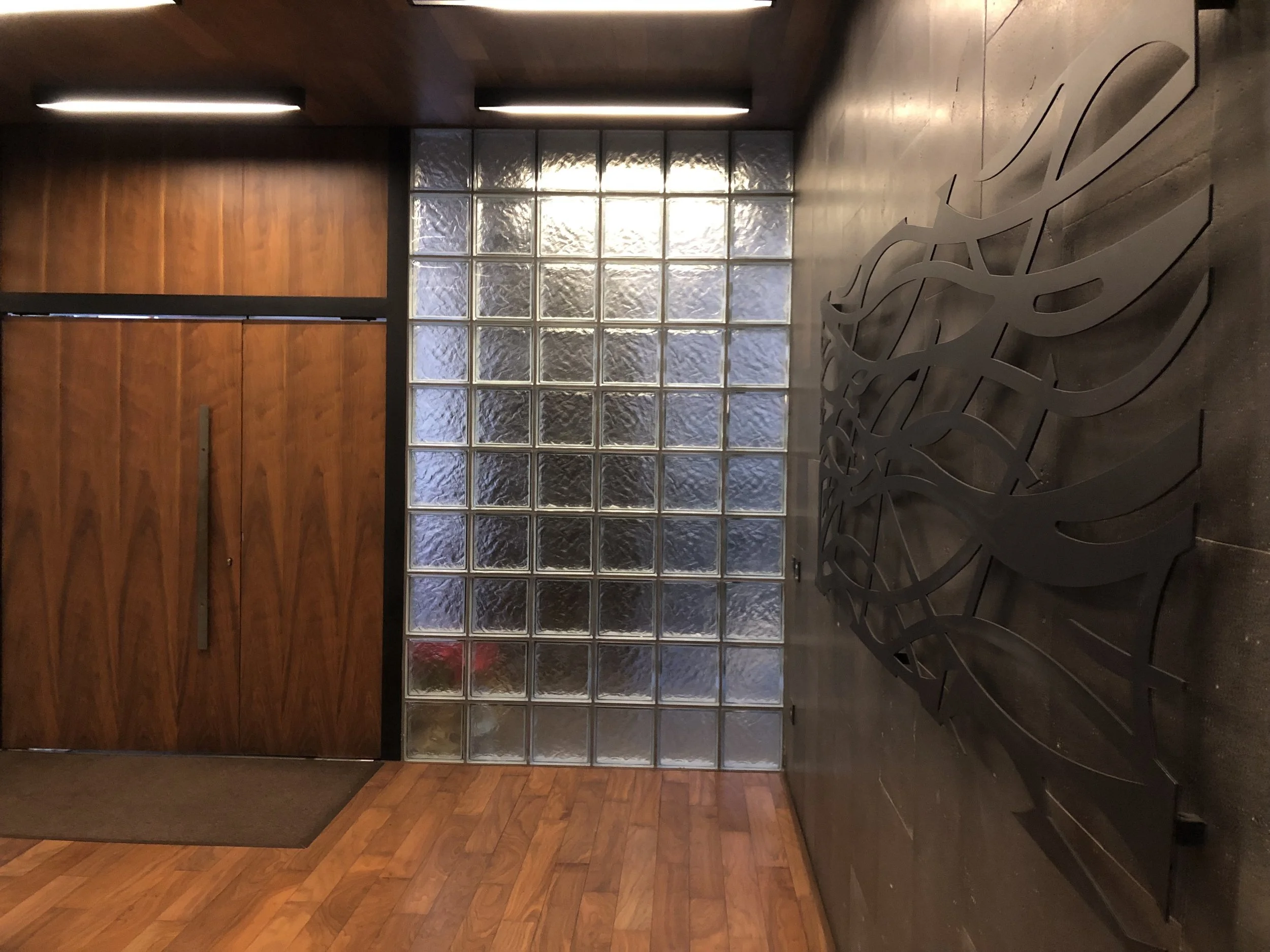 Lobby entrance with wooden door, glass block wall, and decorative metal sculpture on the floor.