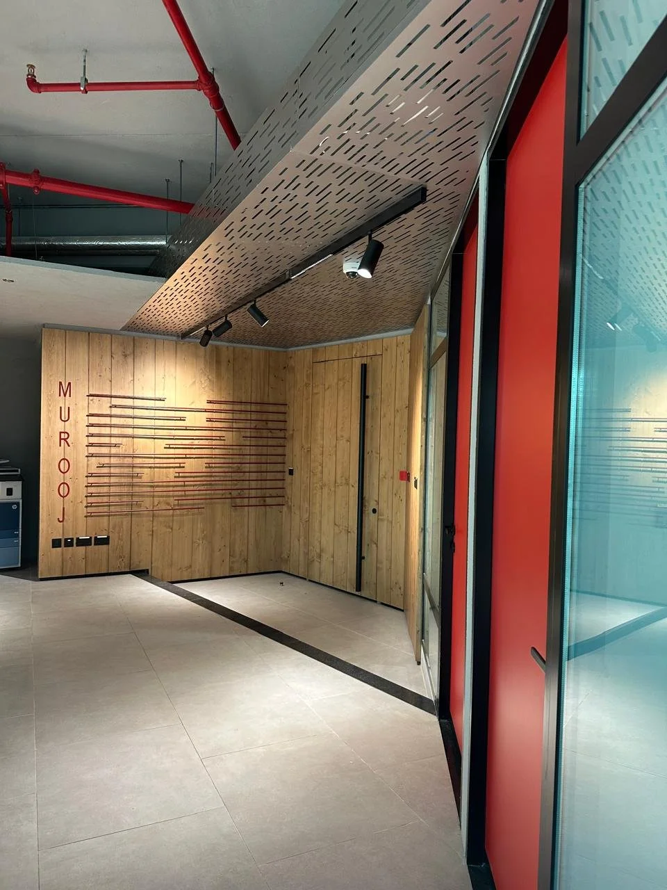 Modern interior with wooden wall displaying various fishing rods, a door, and a large window with red and black framing.
