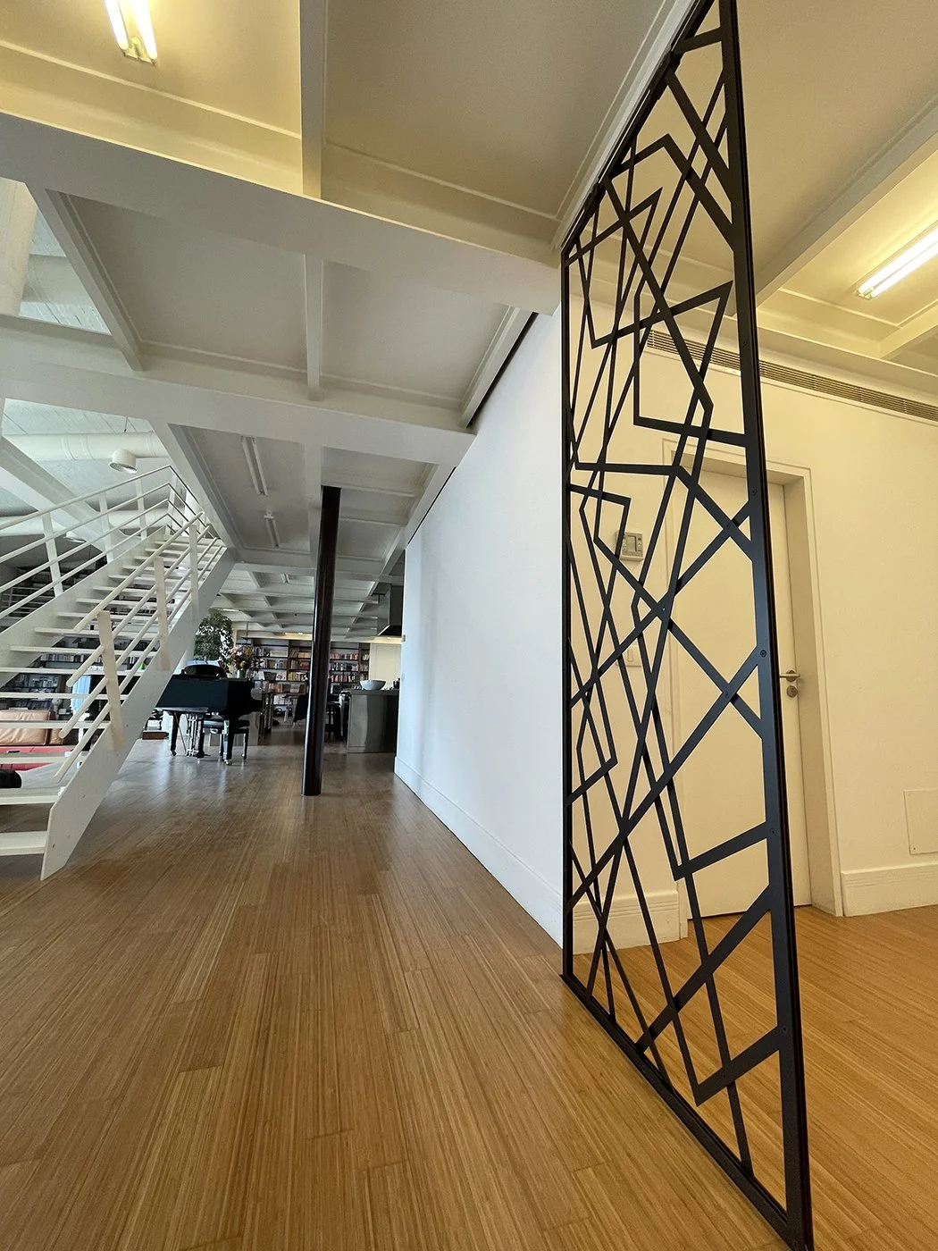 Interior of a modern, spacious building with a wooden floor, metal staircase, and a decorative metal partition.