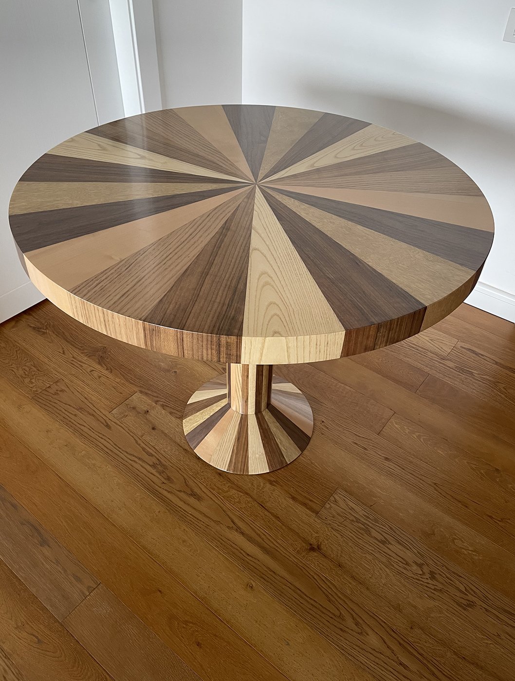 A round wooden table with a geometric pattern on the top using different shades of wood, sitting on a hardwood floor.