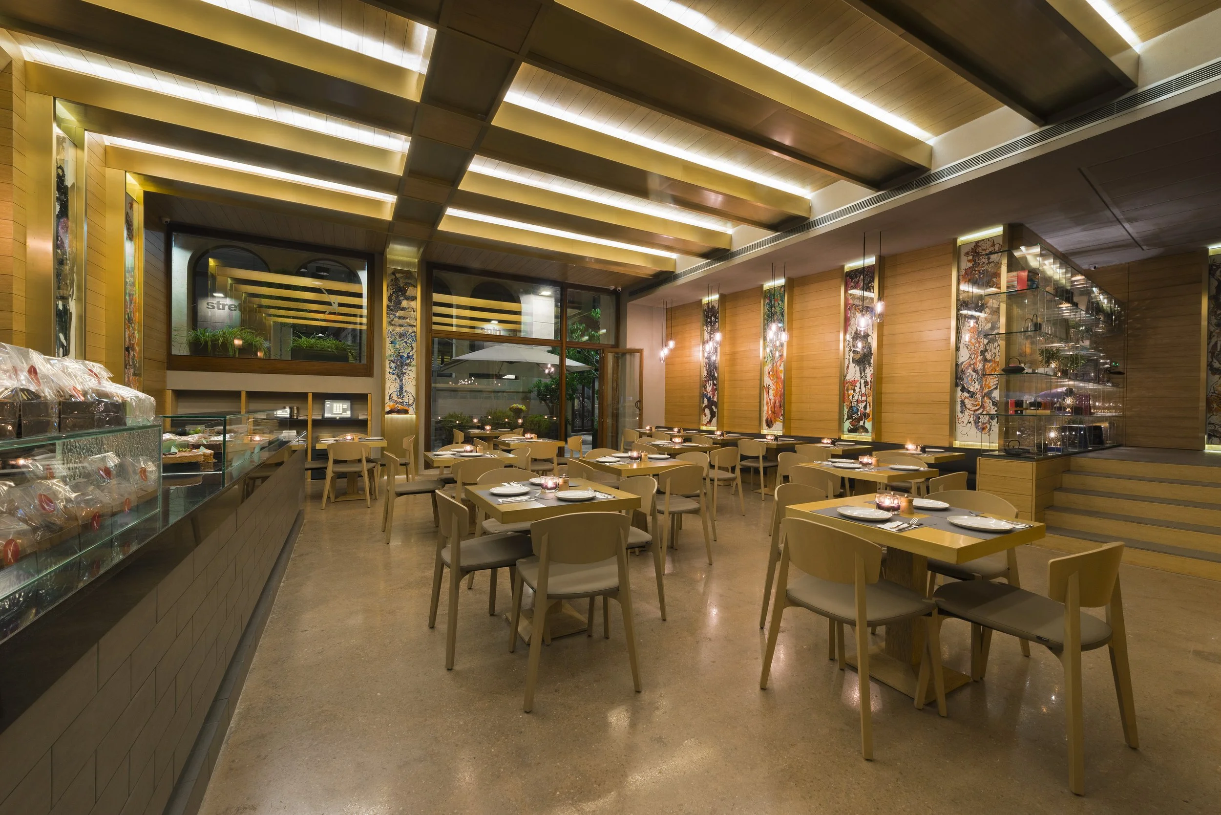 A warmly lit modern restaurant interior with wooden accents, tables set for dining, and decorative hanging lights.