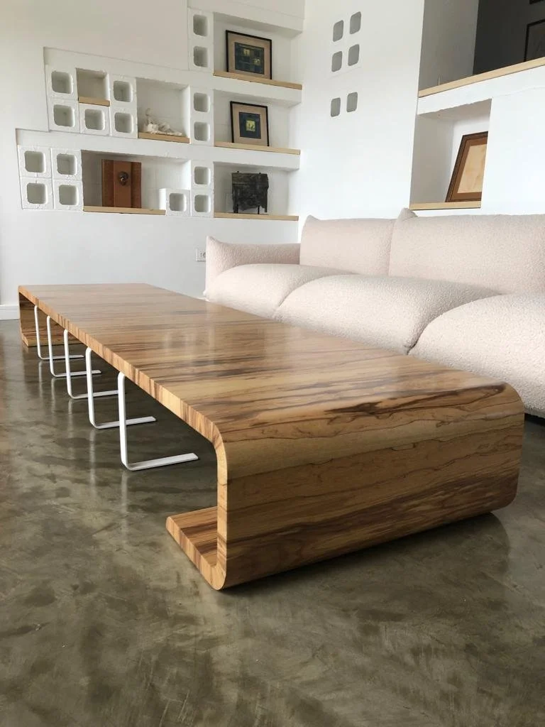 Modern living room with a large wooden table, white couch, and built-in shelves with artwork and decorative objects.