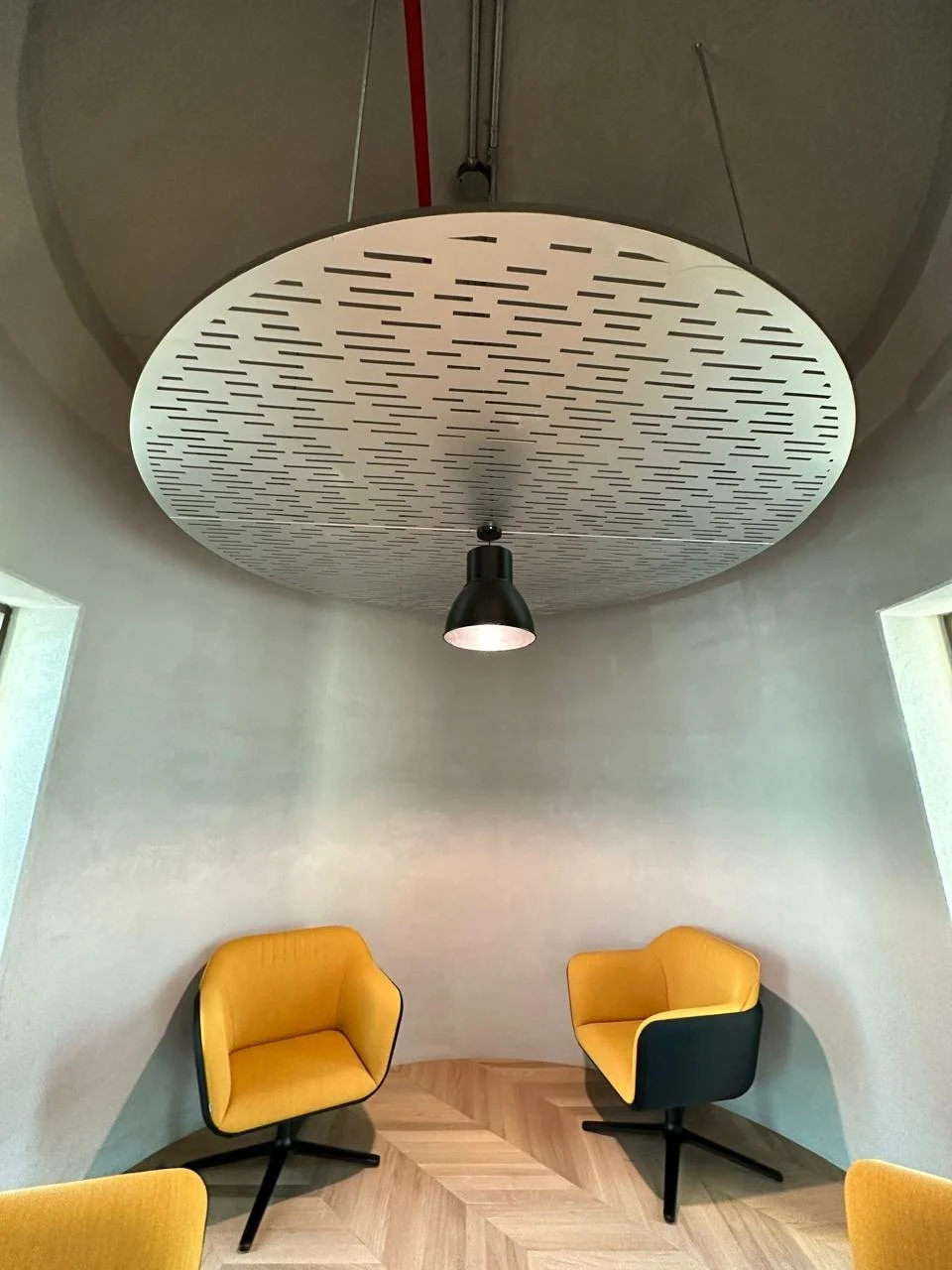 A modern room with yellow lounge chairs, a circular acoustic ceiling panel, and a black pendant light.