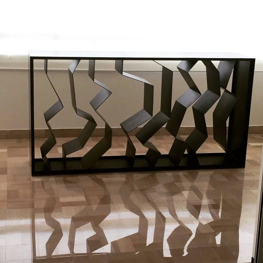 A black metal console table with an abstract, geometrically cut-out zigzag pattern in a modern setting.