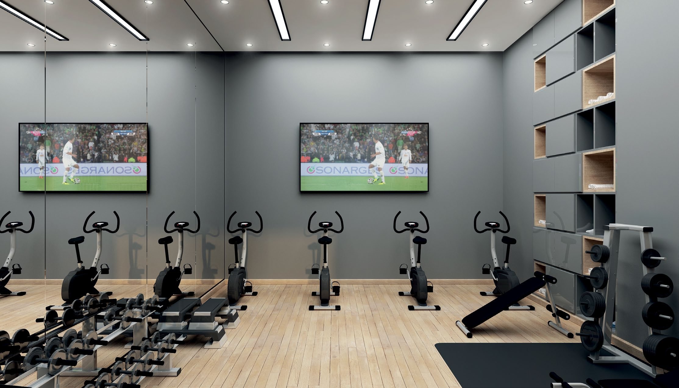 Home gym with six exercise bikes facing a wall-mounted TV showing a soccer game, mirror reflecting part of the room, and shelving with weights and equipment.