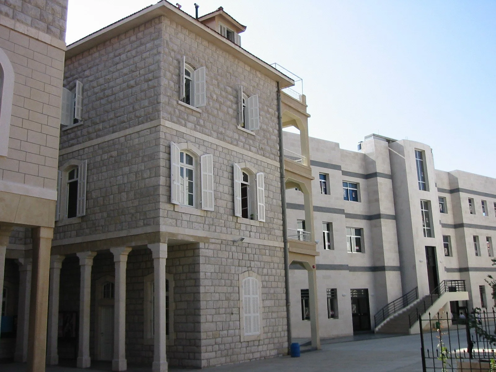 A multi-story building with stone and concrete exterior, several open windows with shutters, and a small balcony, set against a clear sky.