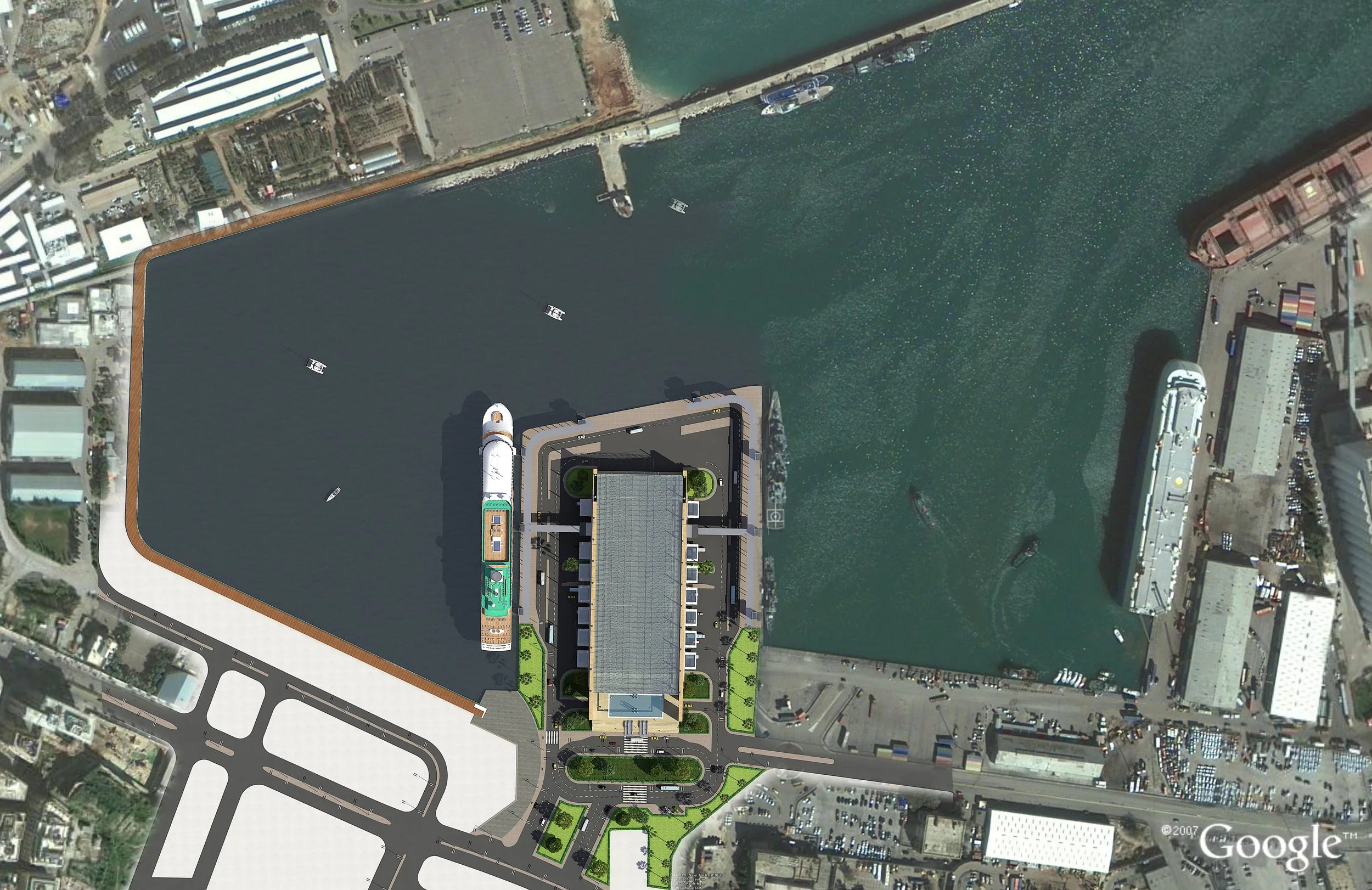 Aerial view of a waterfront development site with water, boats, a large building, and surrounding streets and urban area.
