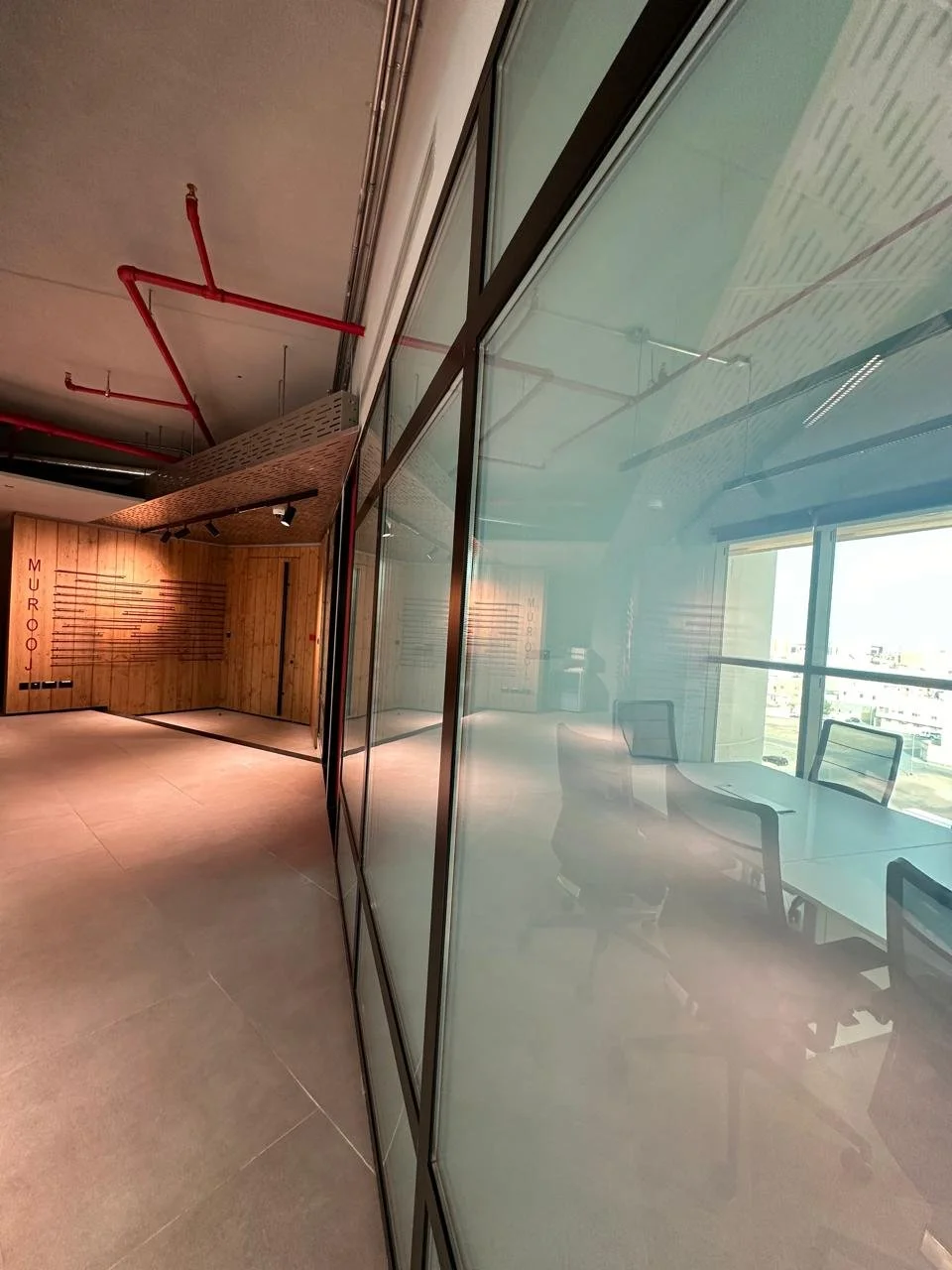 Modern office space with glass walls, a conference table with chairs, and a wall with wooden paneling and the word 'Muroo' in red letters.