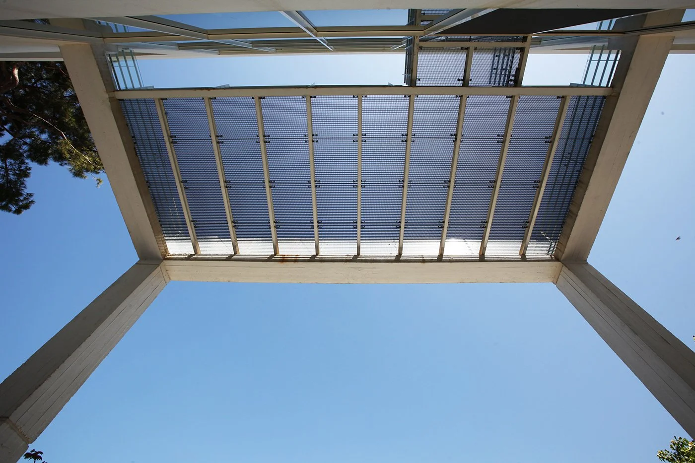 Looking up at the underside of a modern building's exterior balcony or roof structure with blue sky in the background.