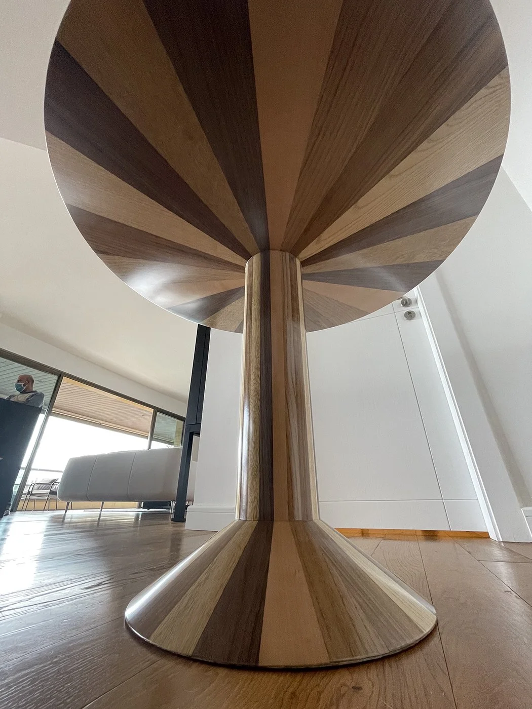 Close-up view of a wooden table with a striped pattern on its underside, standing on a wooden floor in a modern interior space.