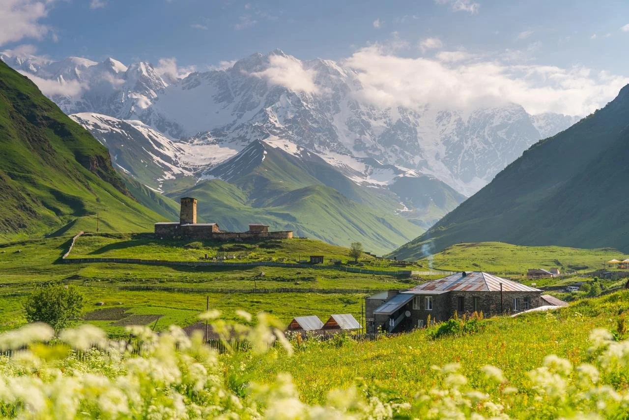 Green valleys with houses and a castle, surrounded by snow-capped mountains in the background.