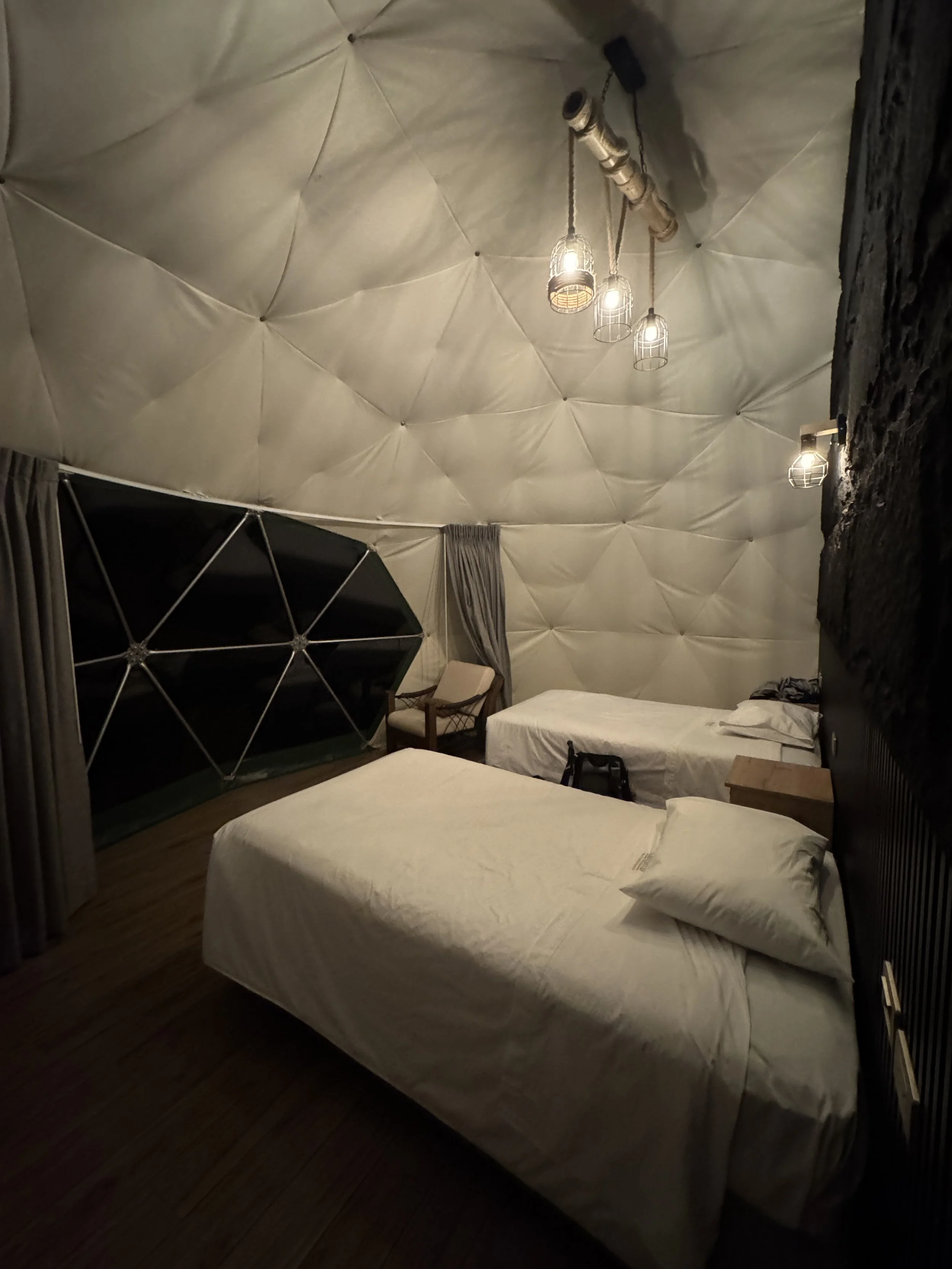 Peru, salkantay trek glass domes. Hotel room with two beds, a chair, side tables, curtains, and unique lighting fixtures on a quilted ceiling.