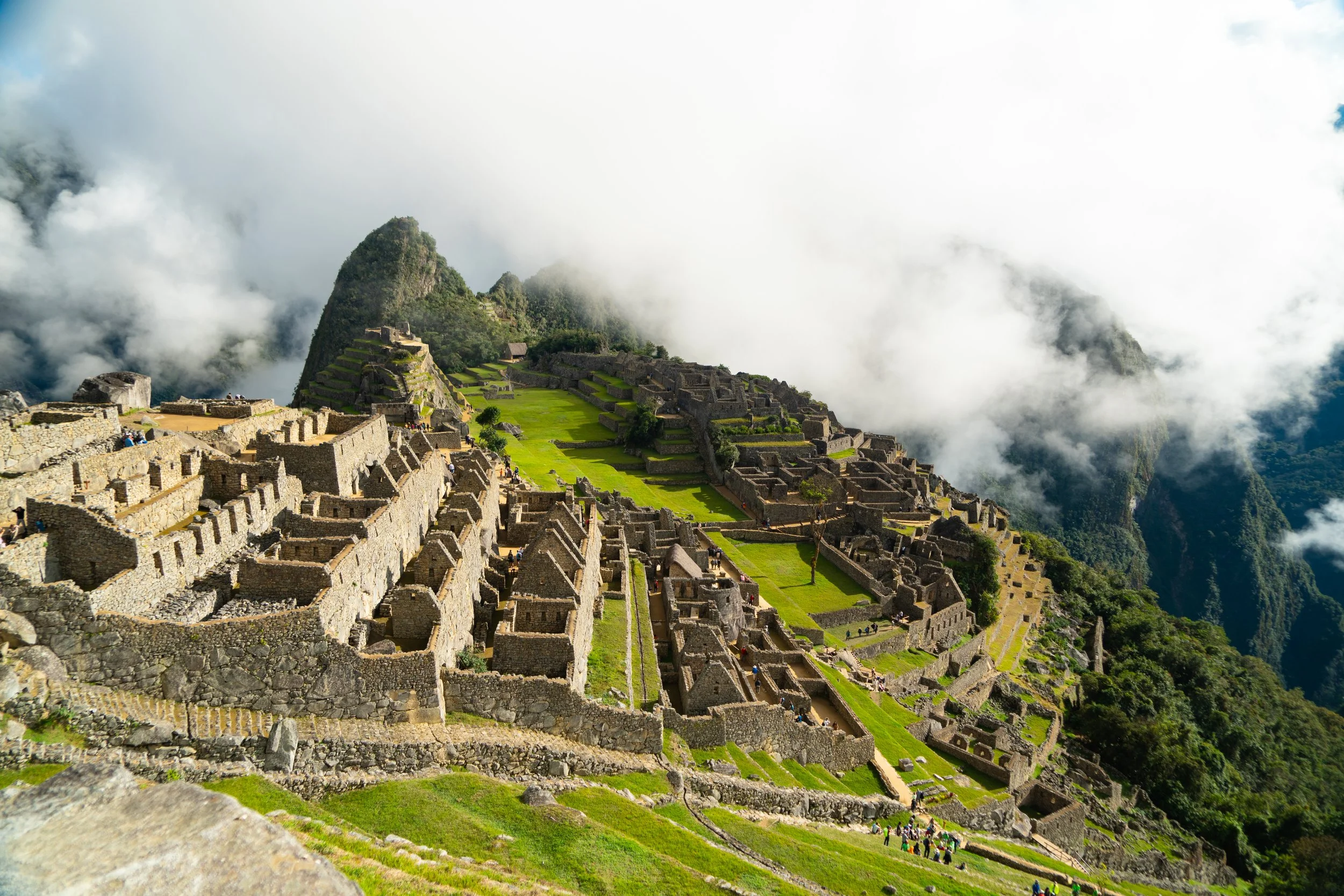 Ancient Incan ruins of Machu Picchu with stone terraces and buildings on a mountain, surrounded by clouds and lush green landscape.