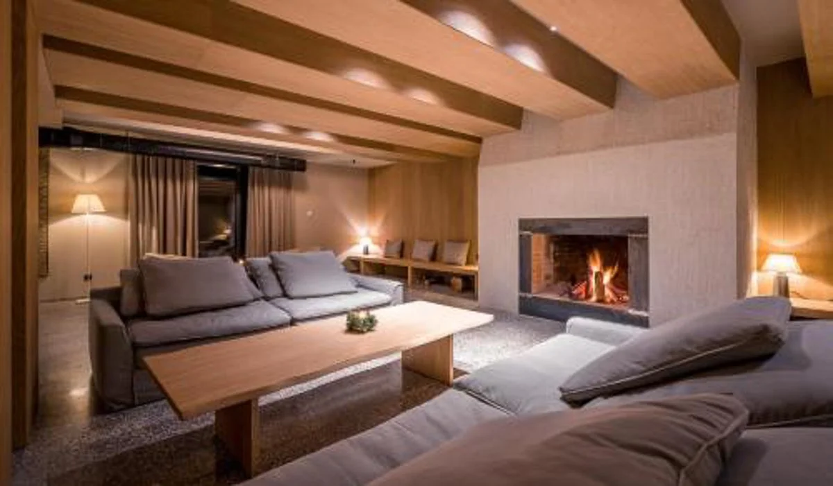 Cozy living room with wooden beams, a fireplace, a large sofa, and warm lighting.