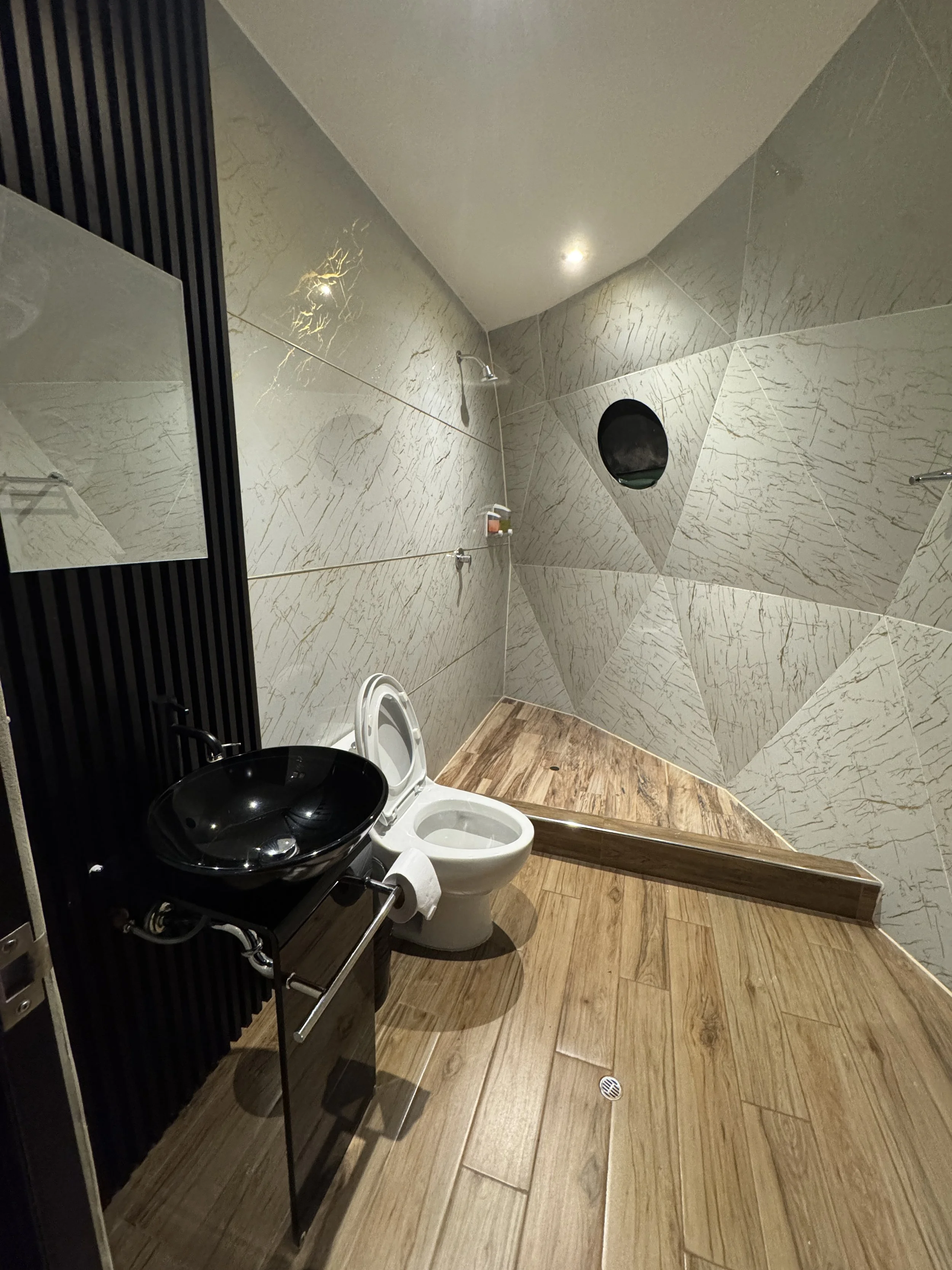 Peru, salkantay Trek glass domes. Modern bathroom with wooden floor, marble wall, black sink, and toilet with open lid.