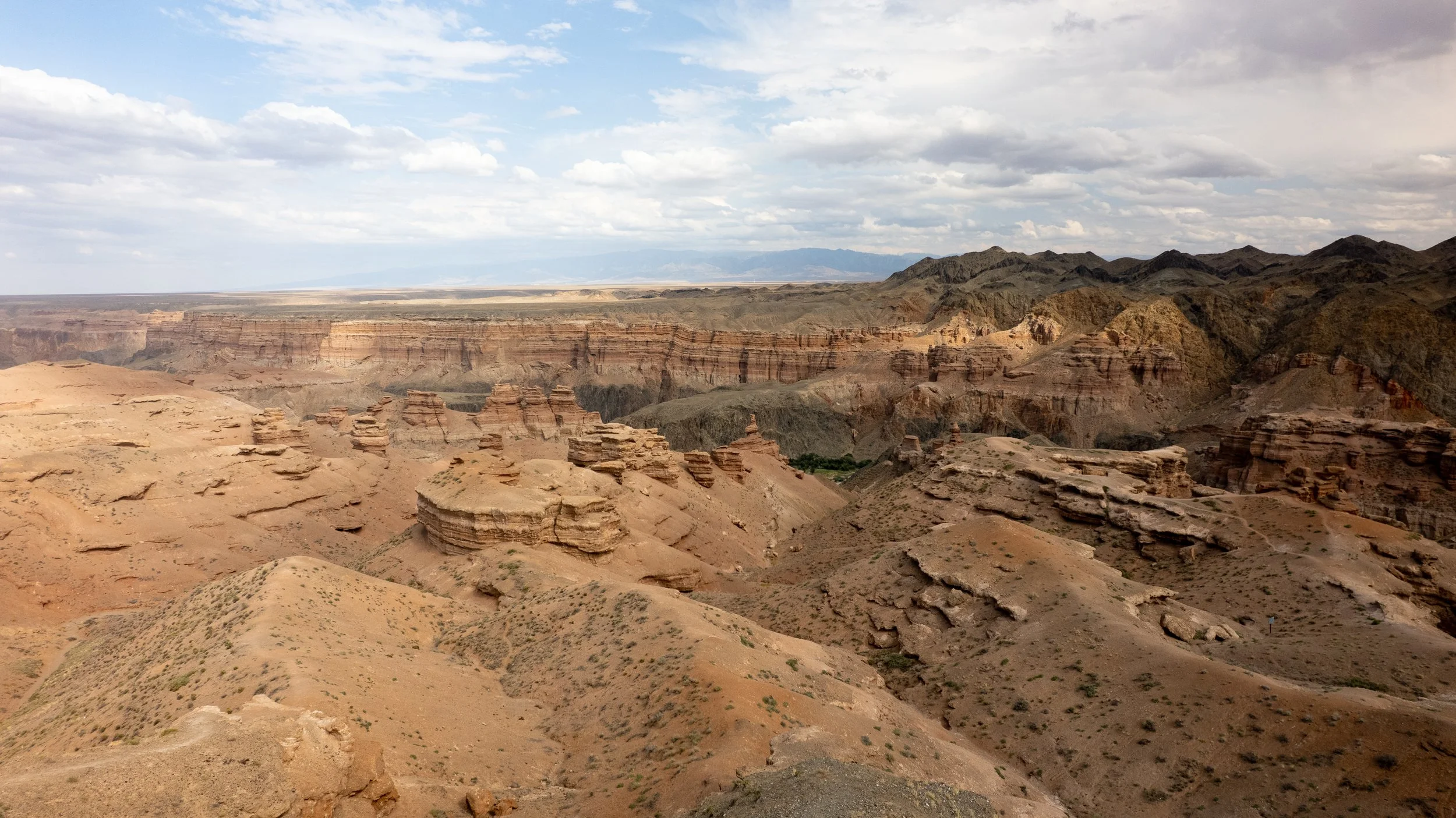 Kazakhstan, charyn canyon. with layered rock formations, rugged terrain, and a partly cloudy sky.