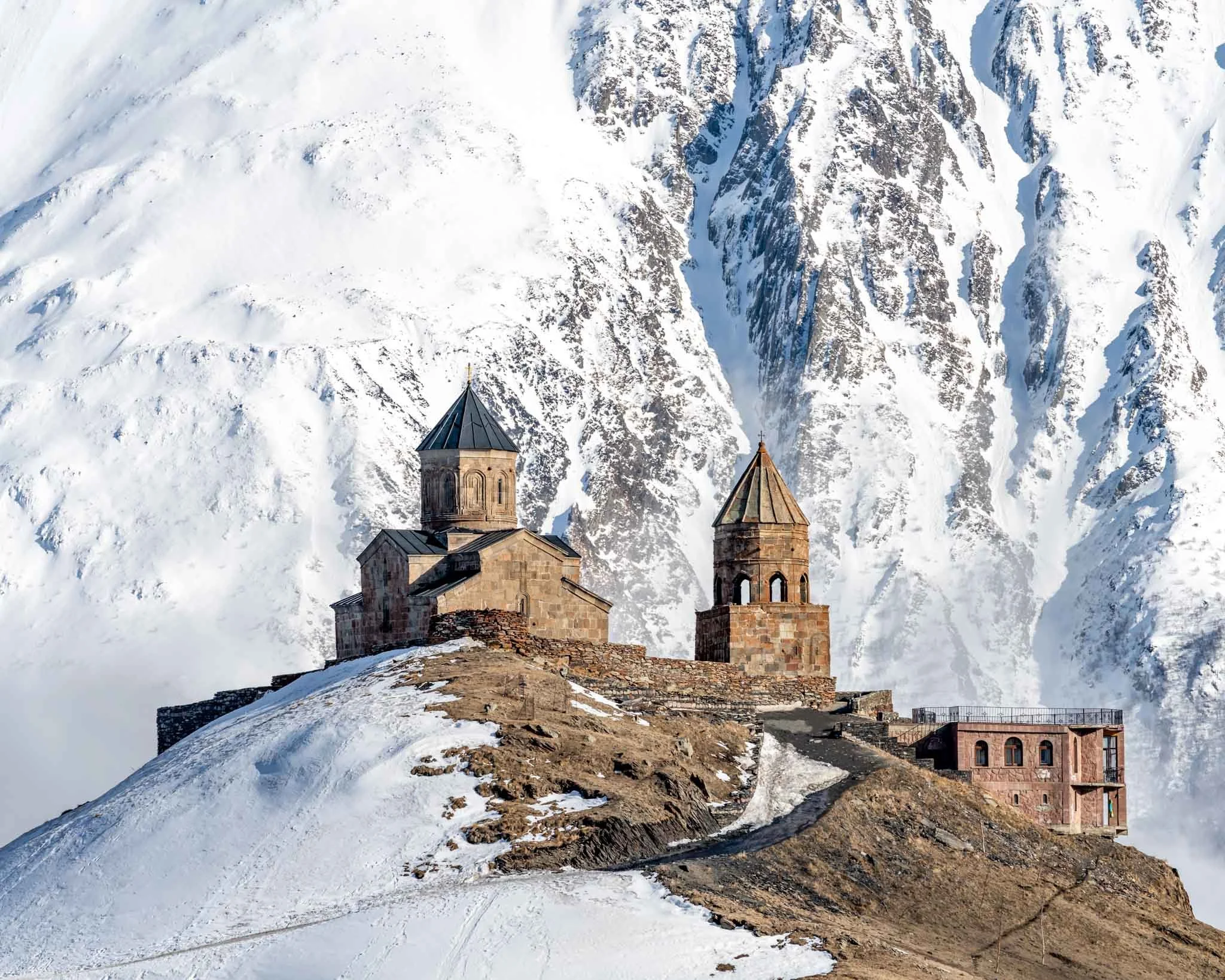 Georgia, Guduari. Ancient stone church on a snow-covered hill with a mountainous, snow-covered background.