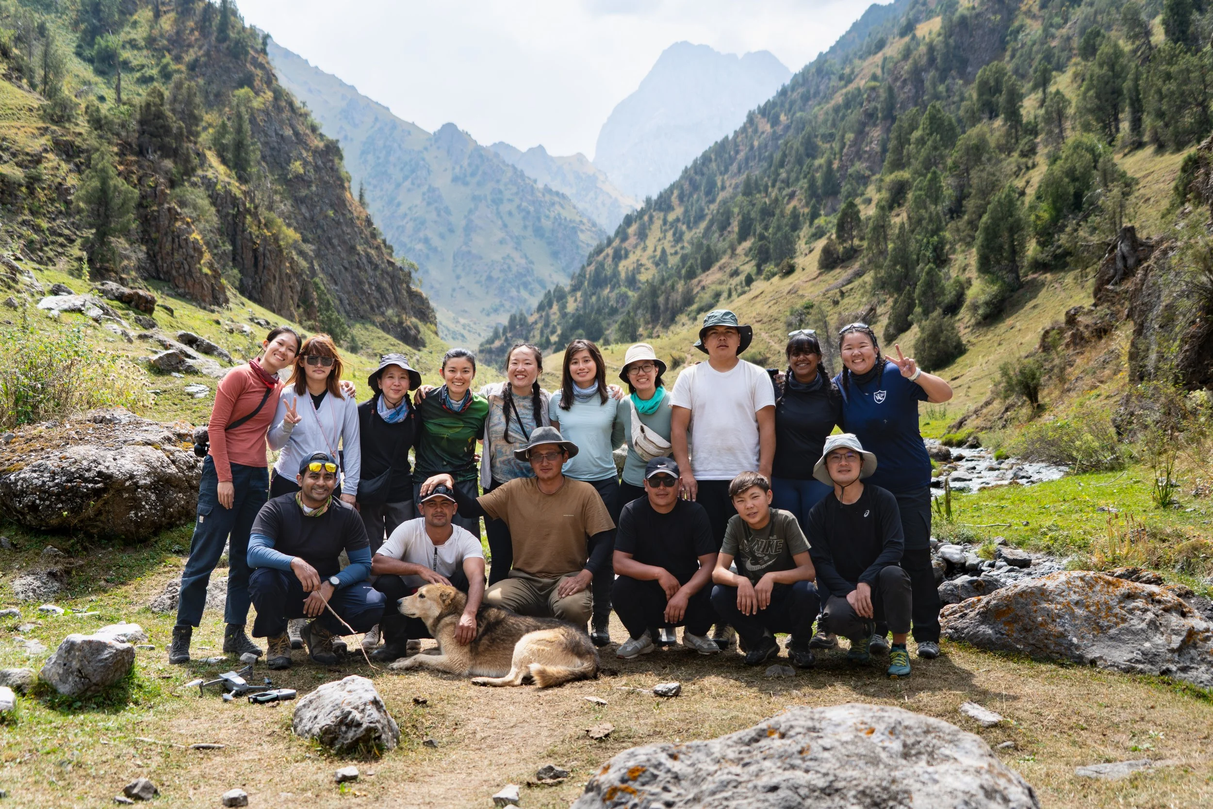 Group of people hiking outdoors in a mountainous area with rocks, trees, and a stream.