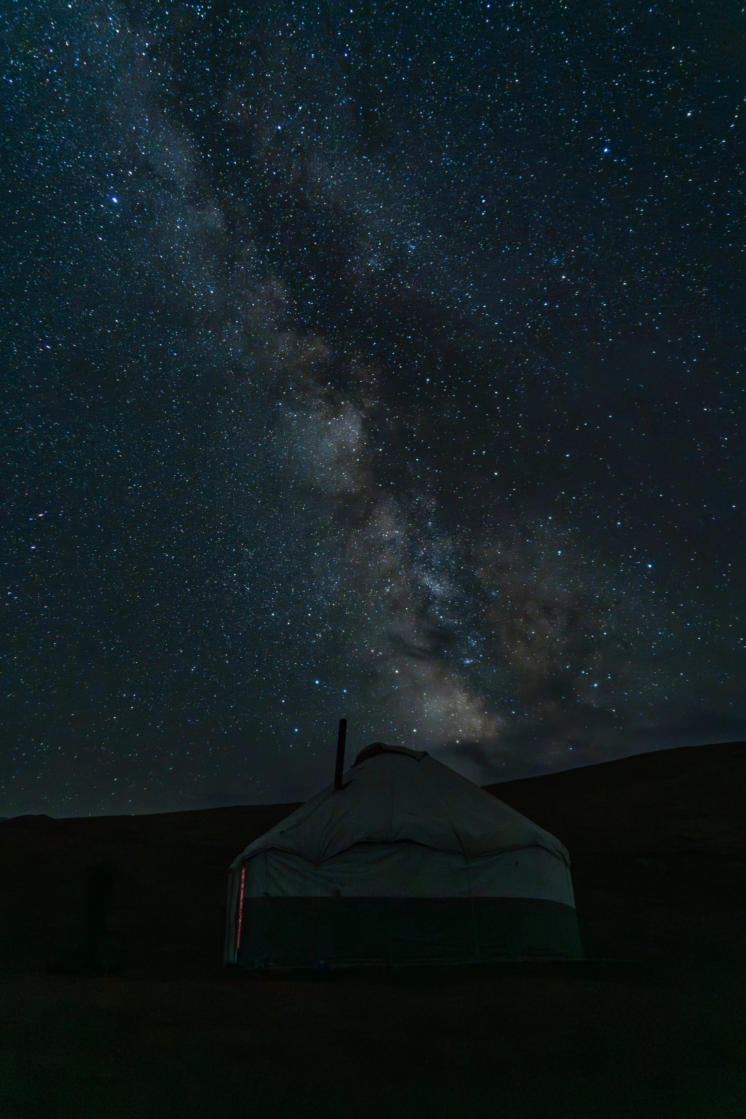 A tent set up outdoors under a night sky filled with stars and the Milky Way galaxy.