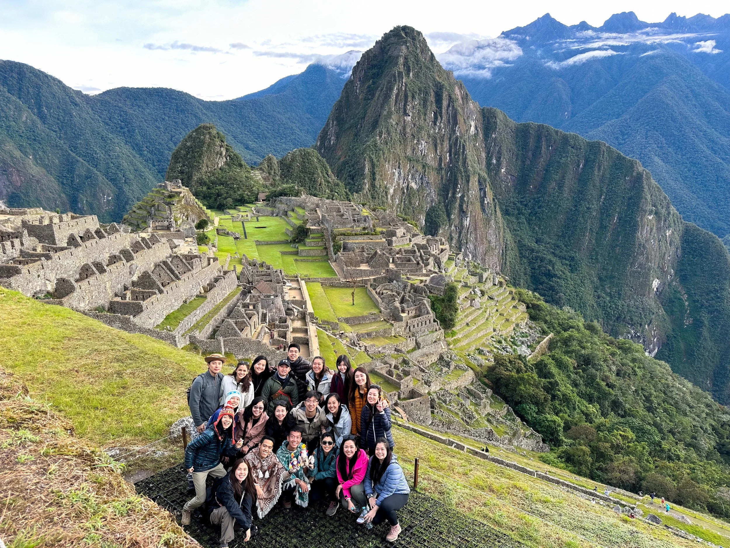 Peru. Group of tourists posing in front of Machu Picchu with terraces and mountains in the background.