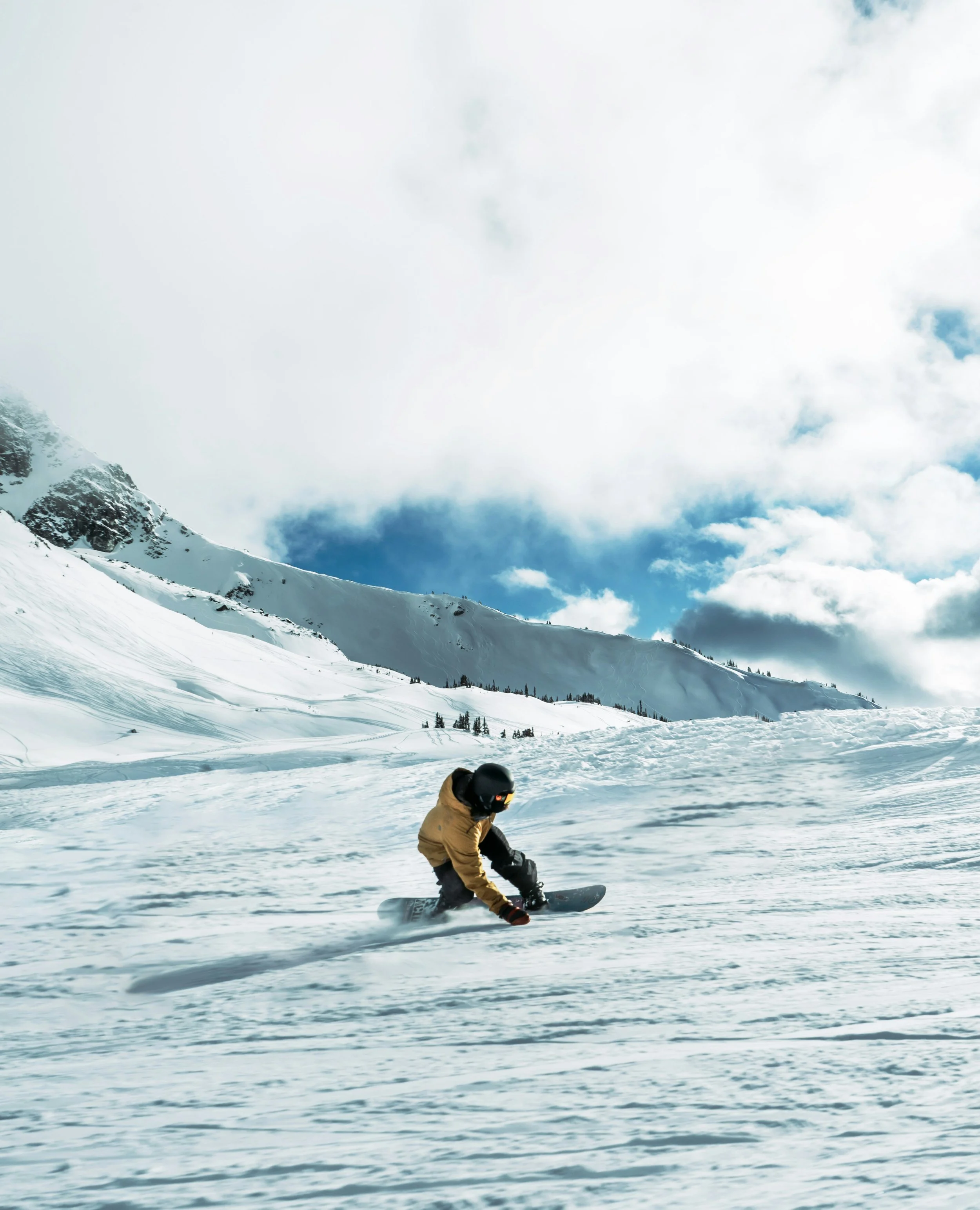 Georgia, Gudauri. A person snowboarding on a snowy mountain slope under a partly cloudy sky.