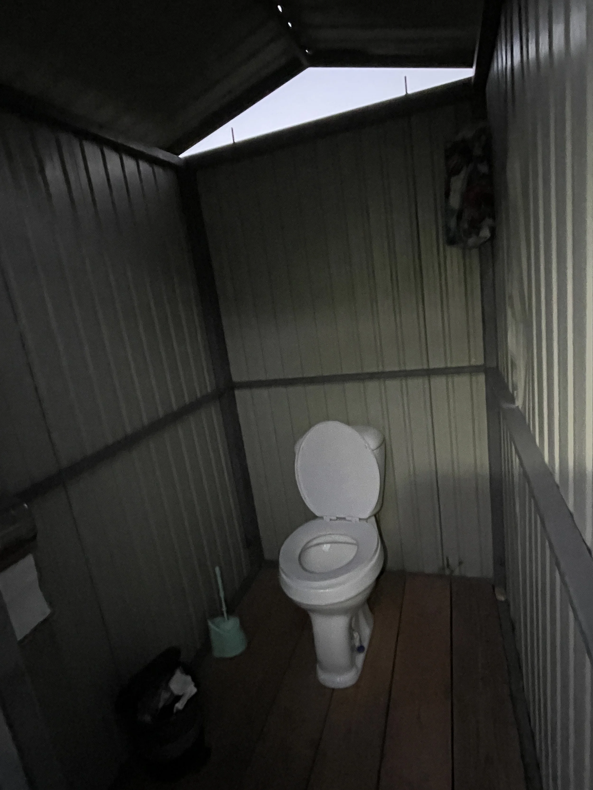 A toilet inside a small, enclosed bathroom with wood-paneled walls and a wooden floor.