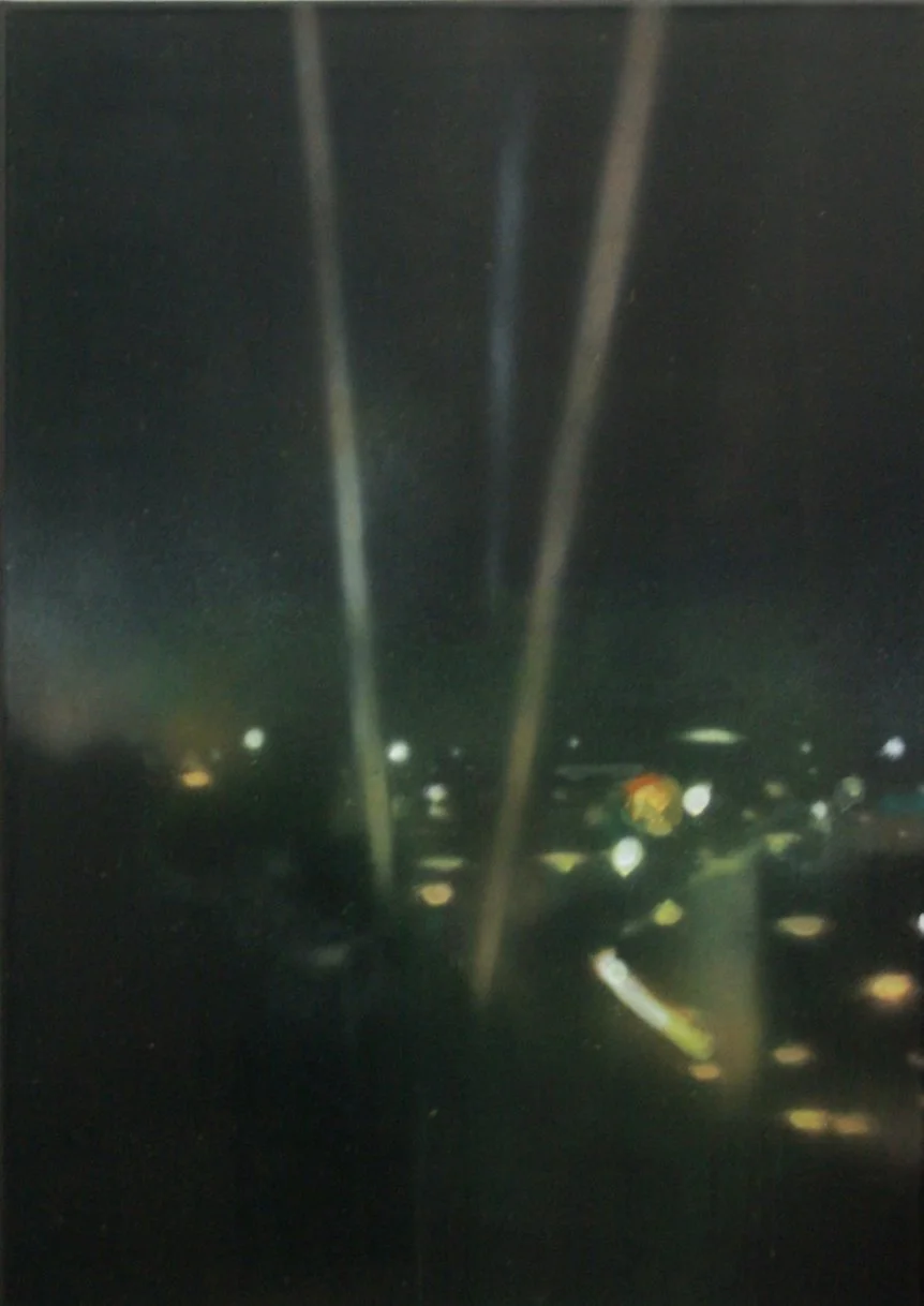 Die Aufnahme zeigt eine dunkle Szenerie mit drei senkrechten, reflektierenden Linien in der Mitte, und verschwommenen Lichtern im Hintergrund, vermutlich Nachtaufnahme einer Stadt.