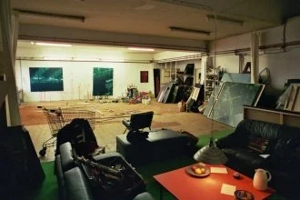 Ein Raum mit mehreren Staffeleien, Kunstwerken und Sitzgelegenheiten, derzeit als Kunststudio oder Atelier genutzt.