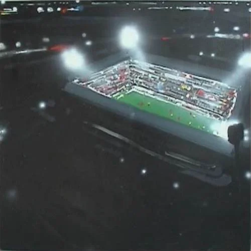 Ein beleuchtetes Fußballstadion bei Nacht, umgeben von Straßen mit Fahrzeuglichtern.