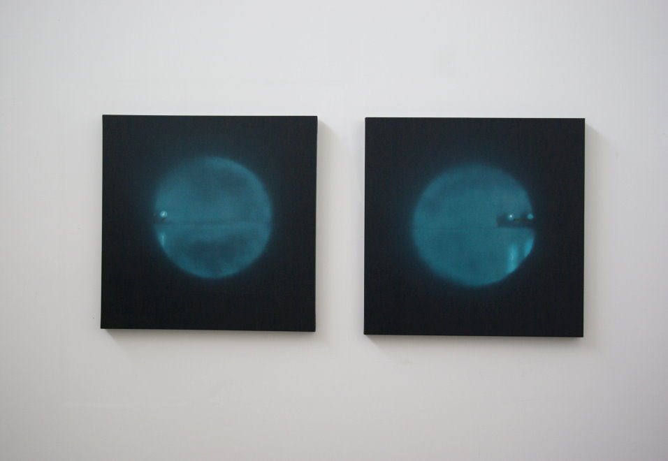 Zwei dunkle quadratische Gemälde mit blauen, kreisförmigen Mustern, hängend an einer weißen Wand.