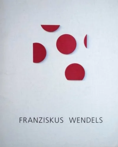 Kunstwerk mit fünf rote, halbkreisförmige und runde Formen an einer weißen Wand, darunter der Text 'FRANZISKUS WENDELS'