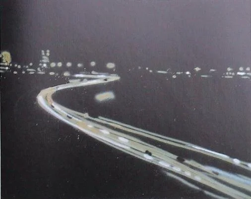 Nachtaufnahme einer kurvigen Straße mit Lichtspuren von fahrenden Autos und Stadtlichtern im Hintergrund.