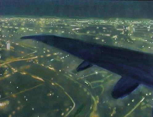 Blick aus einem Flugzeugfenster auf eine Stadt in der Nacht mit beleuchteten Straßen und Gebäuden, Flugzeugflügel sichtbar.