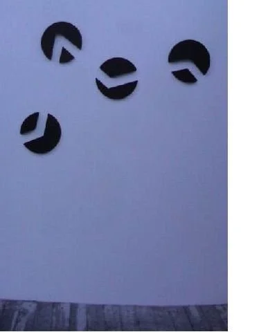 Fünf schwarz ausgeschnittene Kreise mit unterschiedlich angeordneten weißen Linien, an einer weißen Wand befestigt.