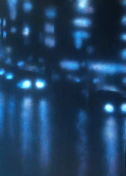 Unklarer, verschwommener Blick auf eine nächtliche Stadtlandschaft mit reflektierenden Lichtern auf Wasser.