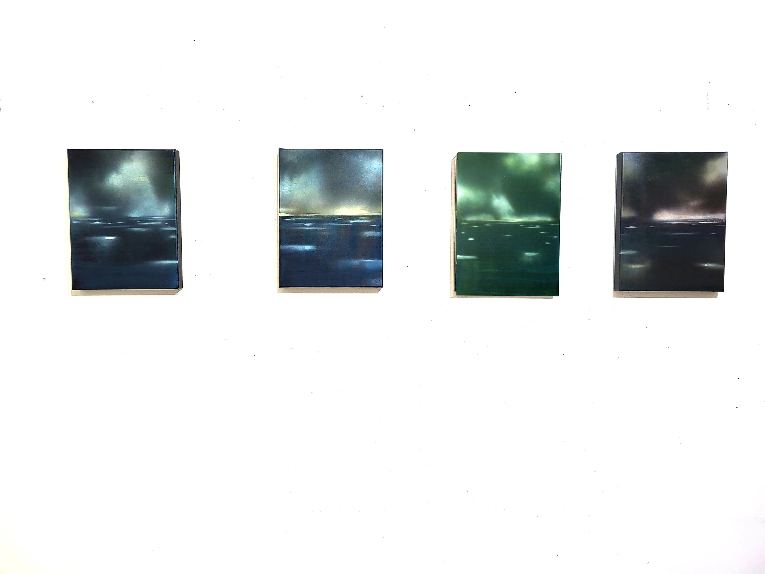Vier quadratische Kunstwerke mit städtischen Landschaften in dunklen Farben, jeweils auf weißem Hintergrund aufgehängt.