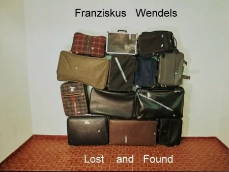 Mehrere Taschen und Koffer sind gegen eine weiße Wand gestellt, mit Name 'Franziskus Wendels' darüber und 'Lost and Found' darunter.