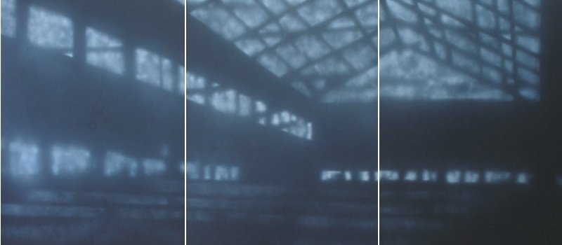 Ansicht eines vernebelten, dunklen industriellen Gebäudes mit sichtbaren Stahlträgern und Fenster in der Ferne.