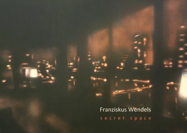 Dunkler Raum mit leuchtenden Lichtern und Holzstühlen, Buchcover von "secret space" von Franziskus Wendel zeigen.
