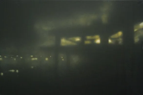 Dunkle, rüttende Szenerie mit einigen Beleuchtungen im Hintergrund, vermutlich eine Unterseite eines Gebäudes oder einer Brücke bei Nacht.