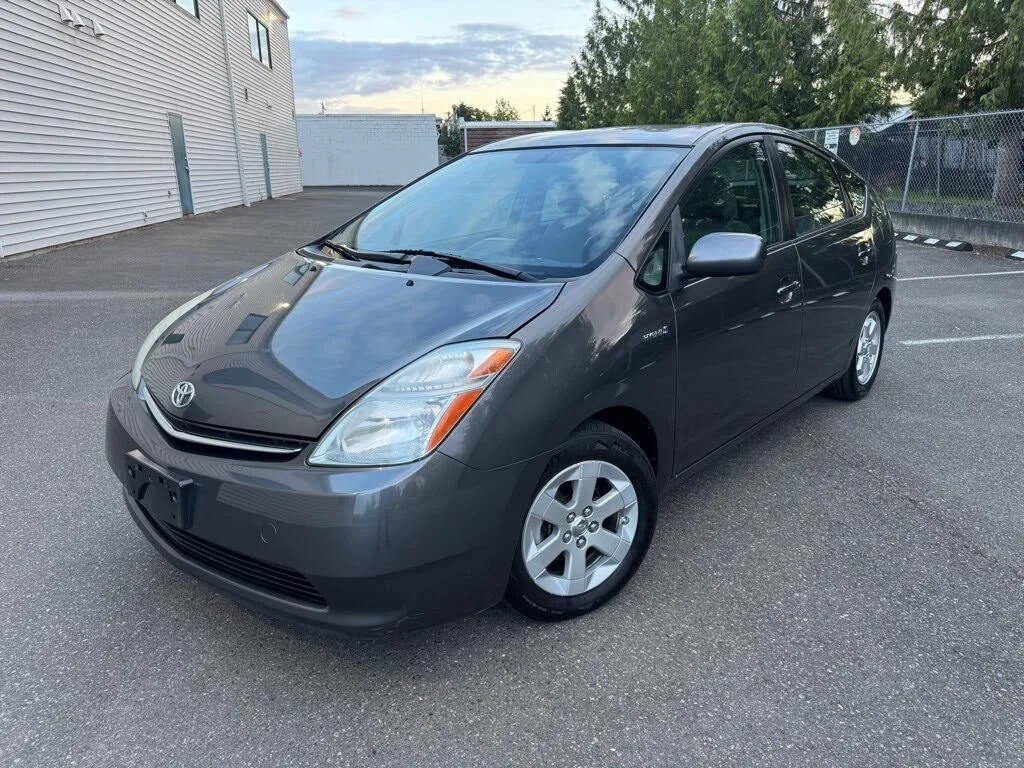 Dark gray Toyota Prius parked in an outdoor lot beside a building and chain-link fence