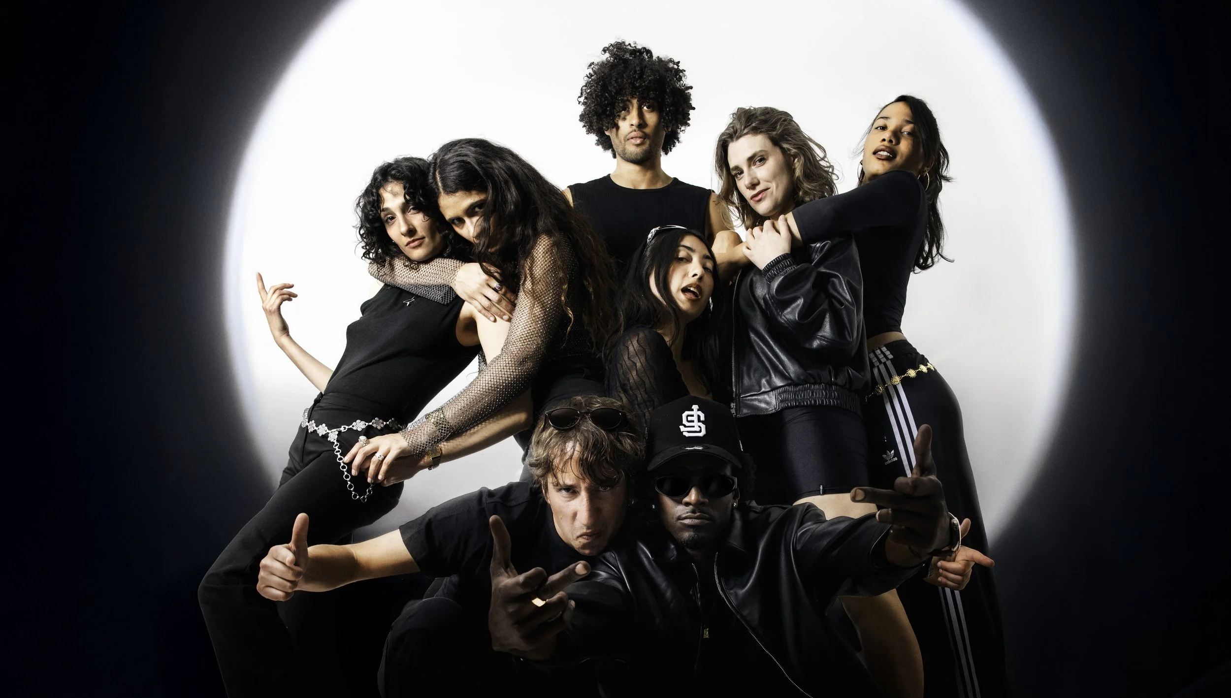 Groupe de huit jeunes adultes posant de manière dynamique devant un fond blanc.