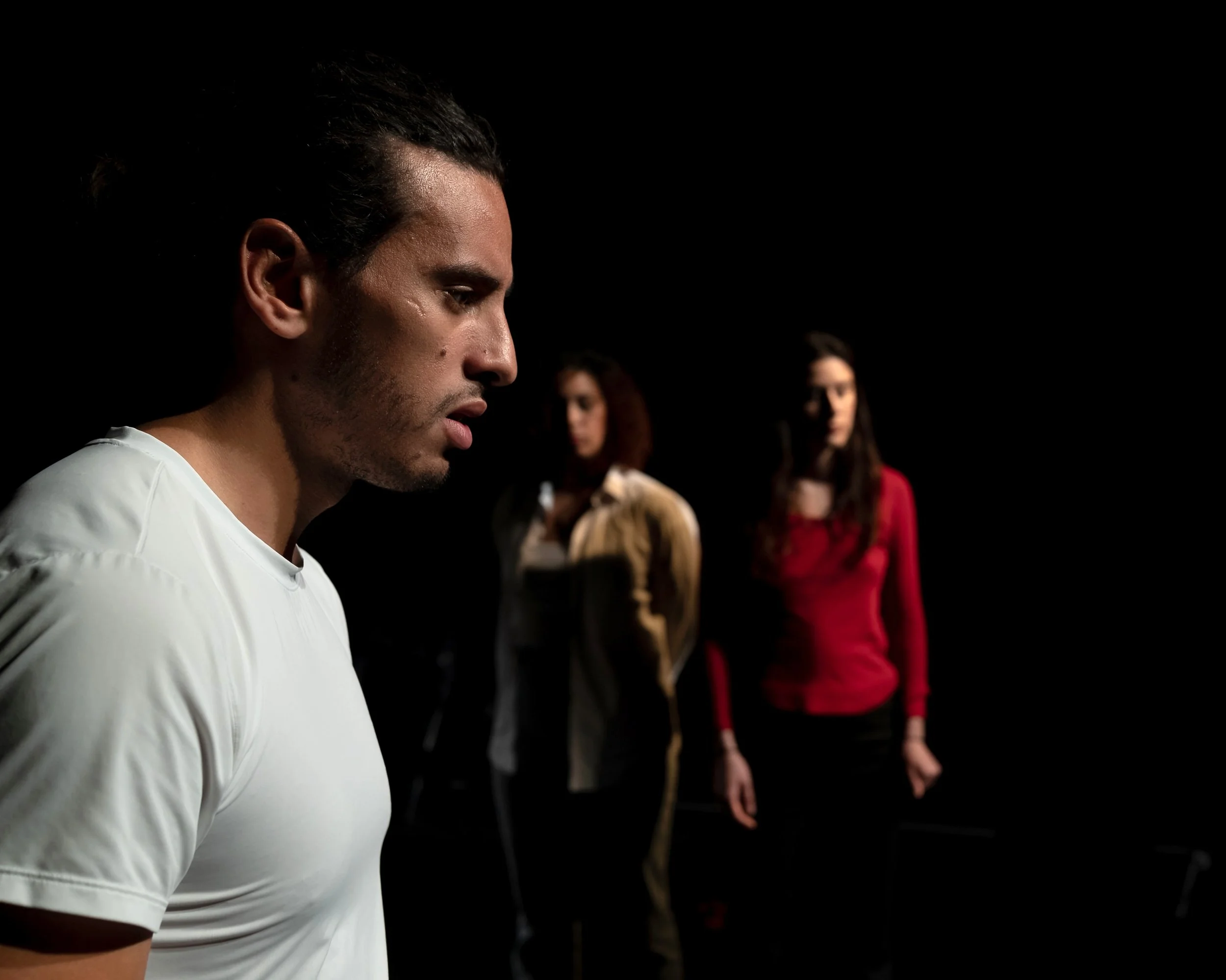 Un homme devant, des femmes en arrière-plan dans un environnement sombre.