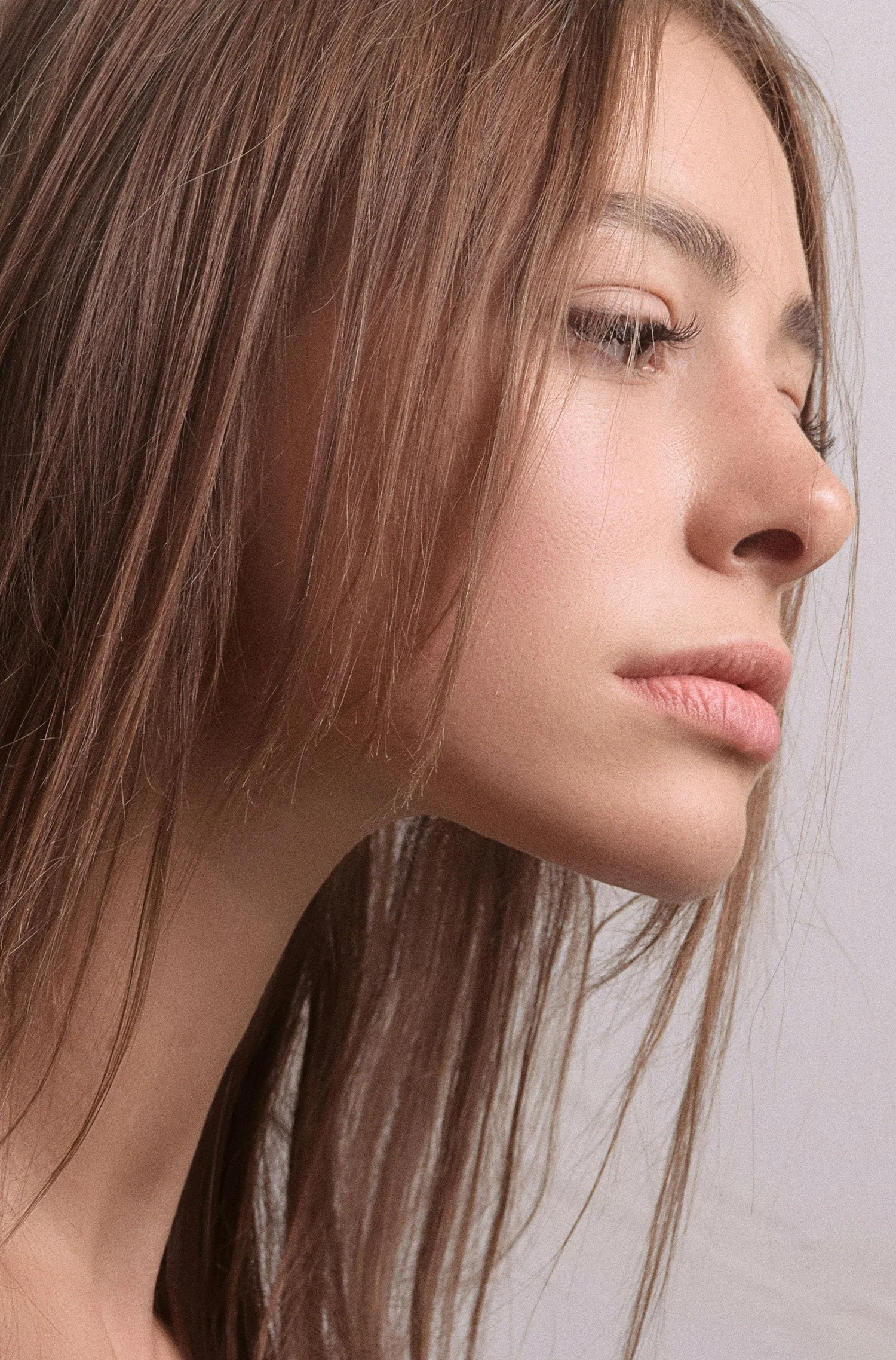 Close-up of a young woman's face in profile with long, brown hair and a neutral expression.