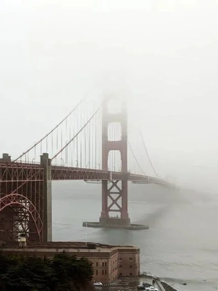 The Golden Gate Bridge partially obscured by thick fog over the water.